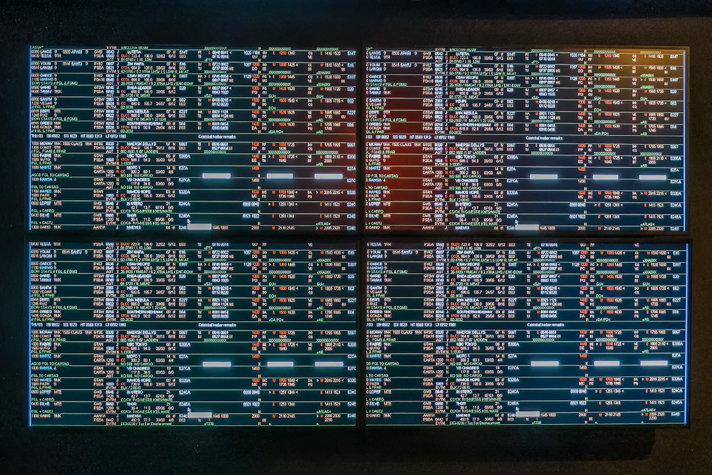 Four computer monitors display rows of complex technical data.